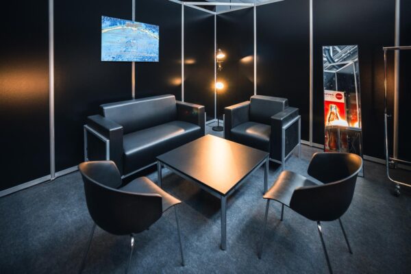 Backstage lounge met zwart evenementenmeubilair: bank, fauteuils, stoelen, salontafel en spiegel – MOJO Rental
